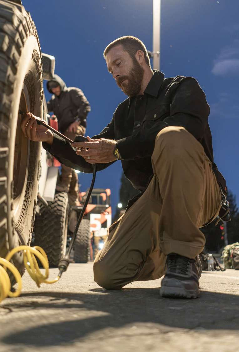 Man crouches next to an off-road wheel well