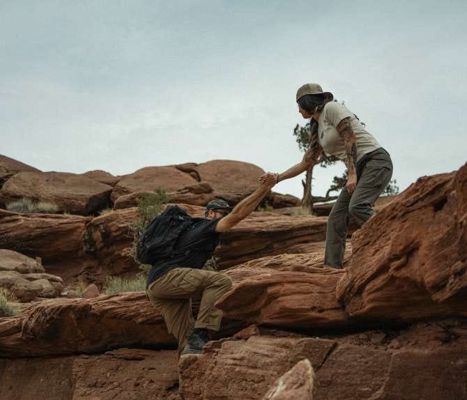 A woman and a man climb up a rocky area