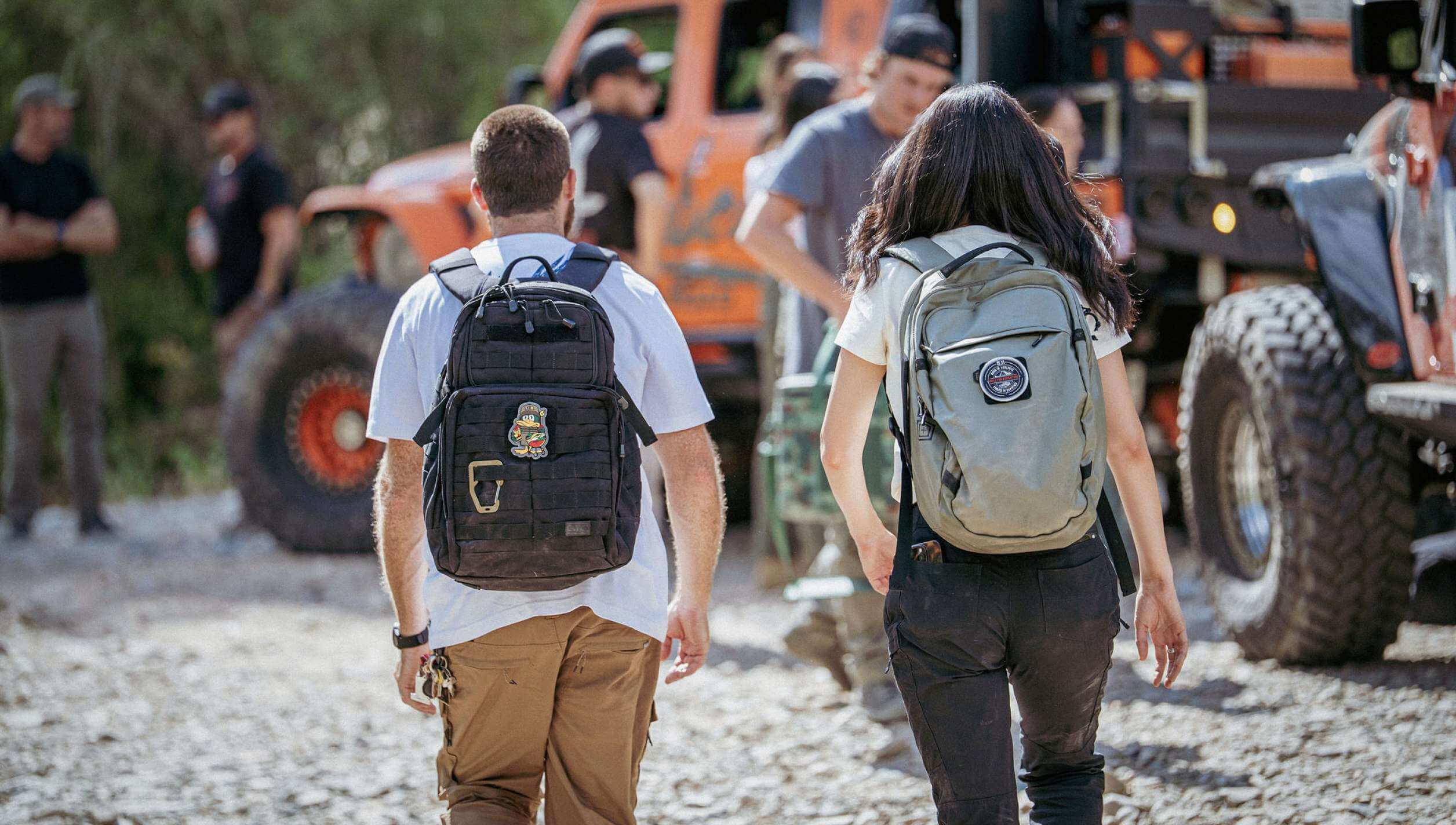 Man wearing RUSH 24 Backpack and a Woman wearing the Allhaula Backpack walk towards a group of off-roaders
