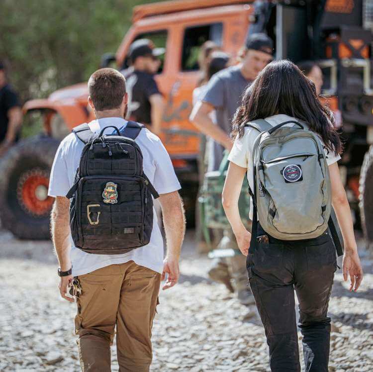 Man wearing RUSH 24 Backpack and a Woman wearing the Allhaula Backpack walk towards a group of off-roaders