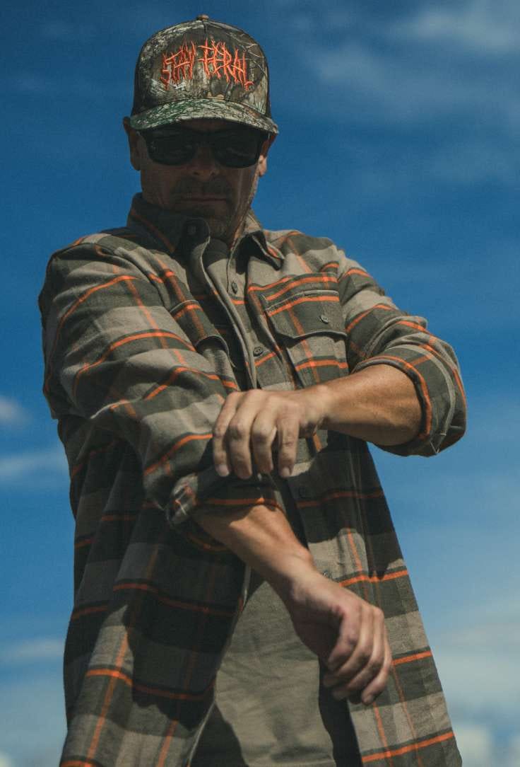 Man in flannel, rolling up sleeve.