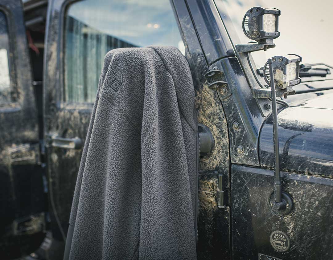 Chaqueta de forro polar colocada sobre un vehículo robusto, destacando su uso como capa para clima frío.