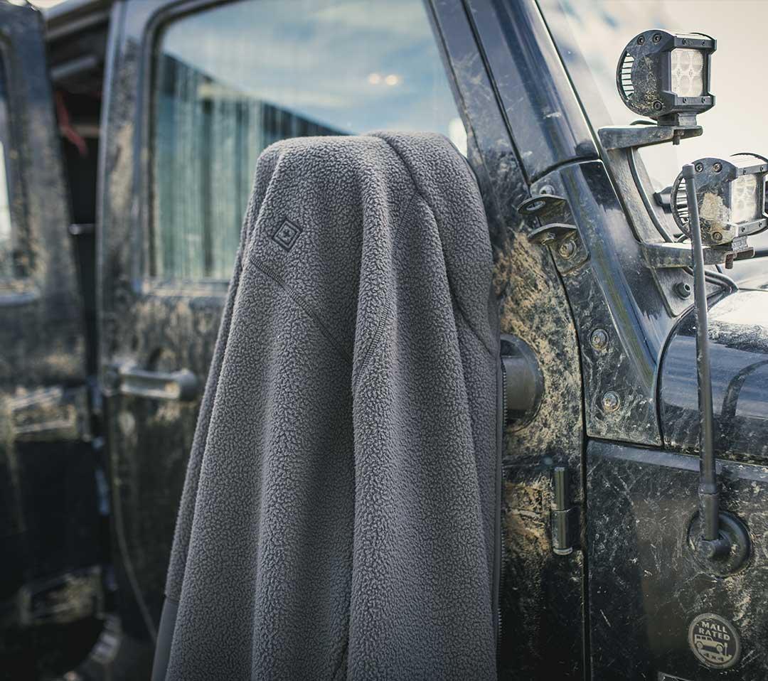 Chaqueta de forro polar colocada sobre un vehículo robusto, destacando su uso como capa para clima frío.