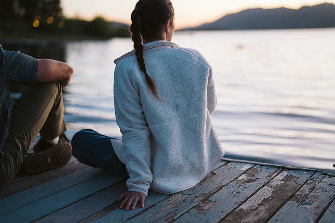 Persona con una chaqueta de forro polar sentada junto al agua al atardecer, mostrando el forro polar como capa exterior versátil.