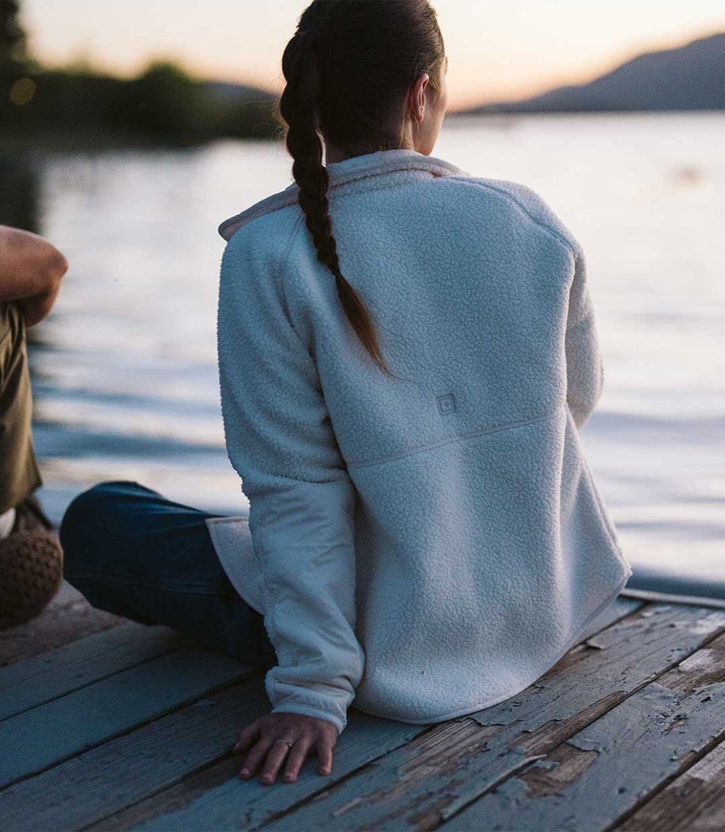 Persona con una chaqueta de forro polar sentada junto al agua al atardecer, mostrando el forro polar como capa exterior versátil.