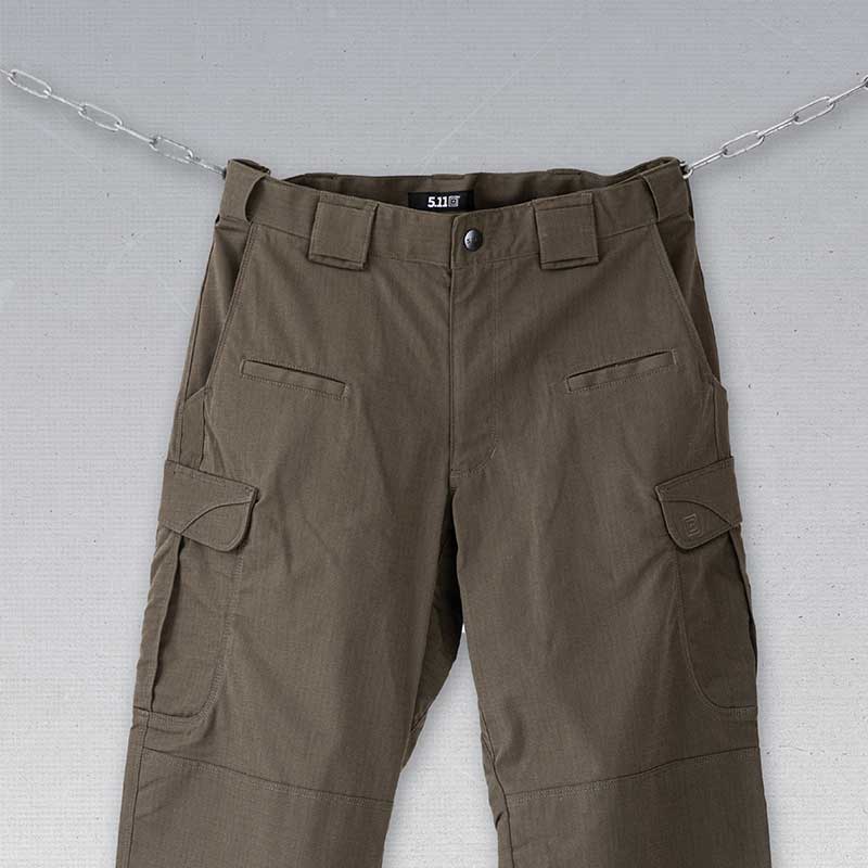 Das Bild zeigt ein Paar 5.11 Stryke Cargo-Hosen in Ranger Green, die an Ketten h&auml;ngen.