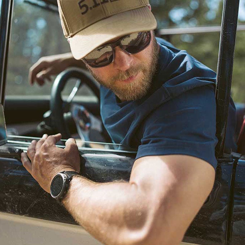 A man in a car wearing a blue 5.11 T-shirt, looking out the window as he is backing.